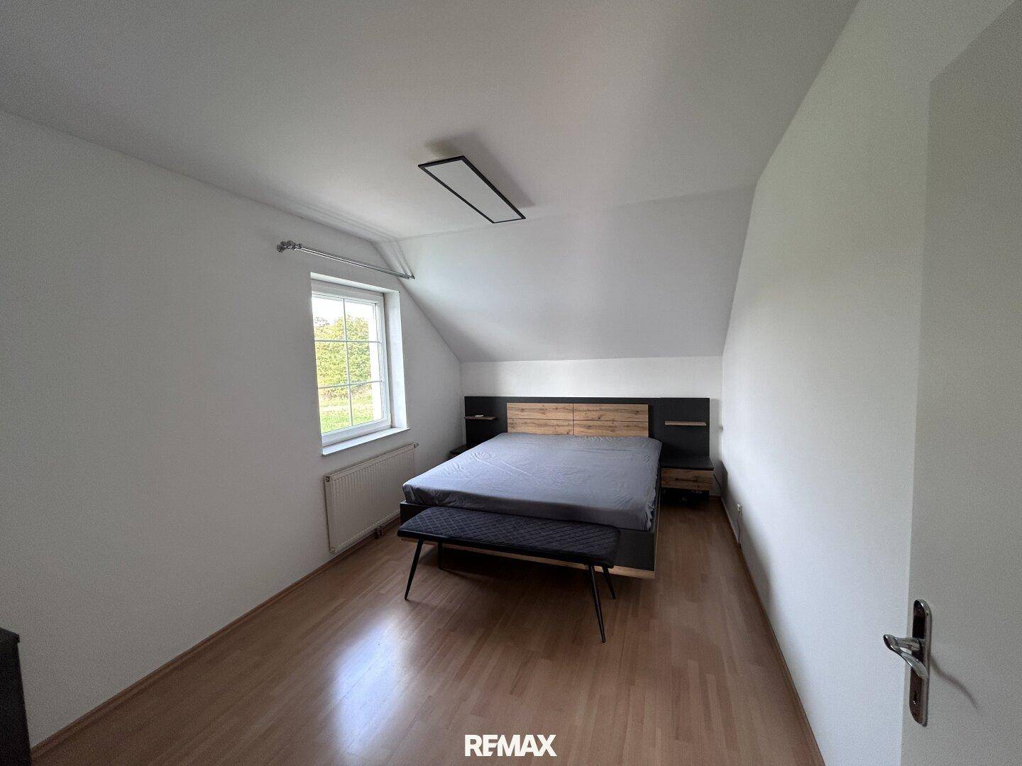Helles Schlafzimmer mit Holzbett, Parkettboden und Fenster, bietet eine ruhige Atmosphäre unter der Dachschräge.