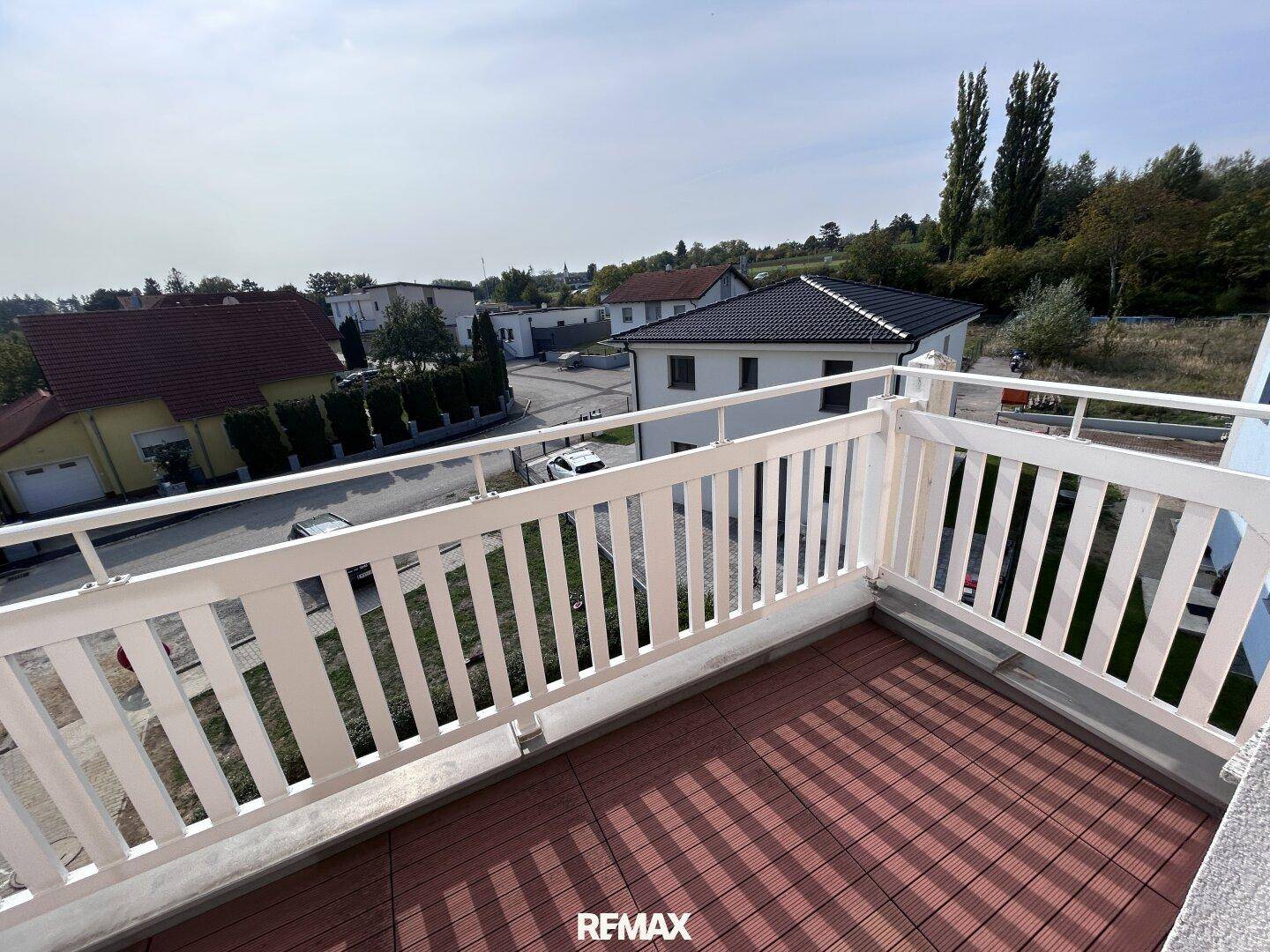 Geräumiger Balkon mit weißem Geländer und Holzboden, bietet einen weiten Blick über die Wohngegend.