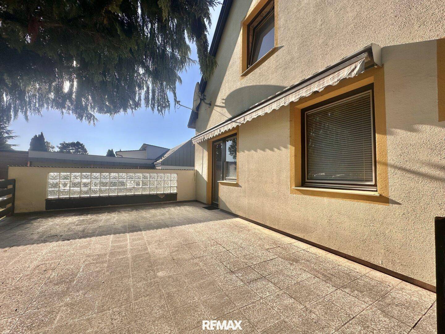 Gedeckte Terrasse mit Fliesenboden und Glasbausteinwand, ideal für entspannte Stunden im Freien.