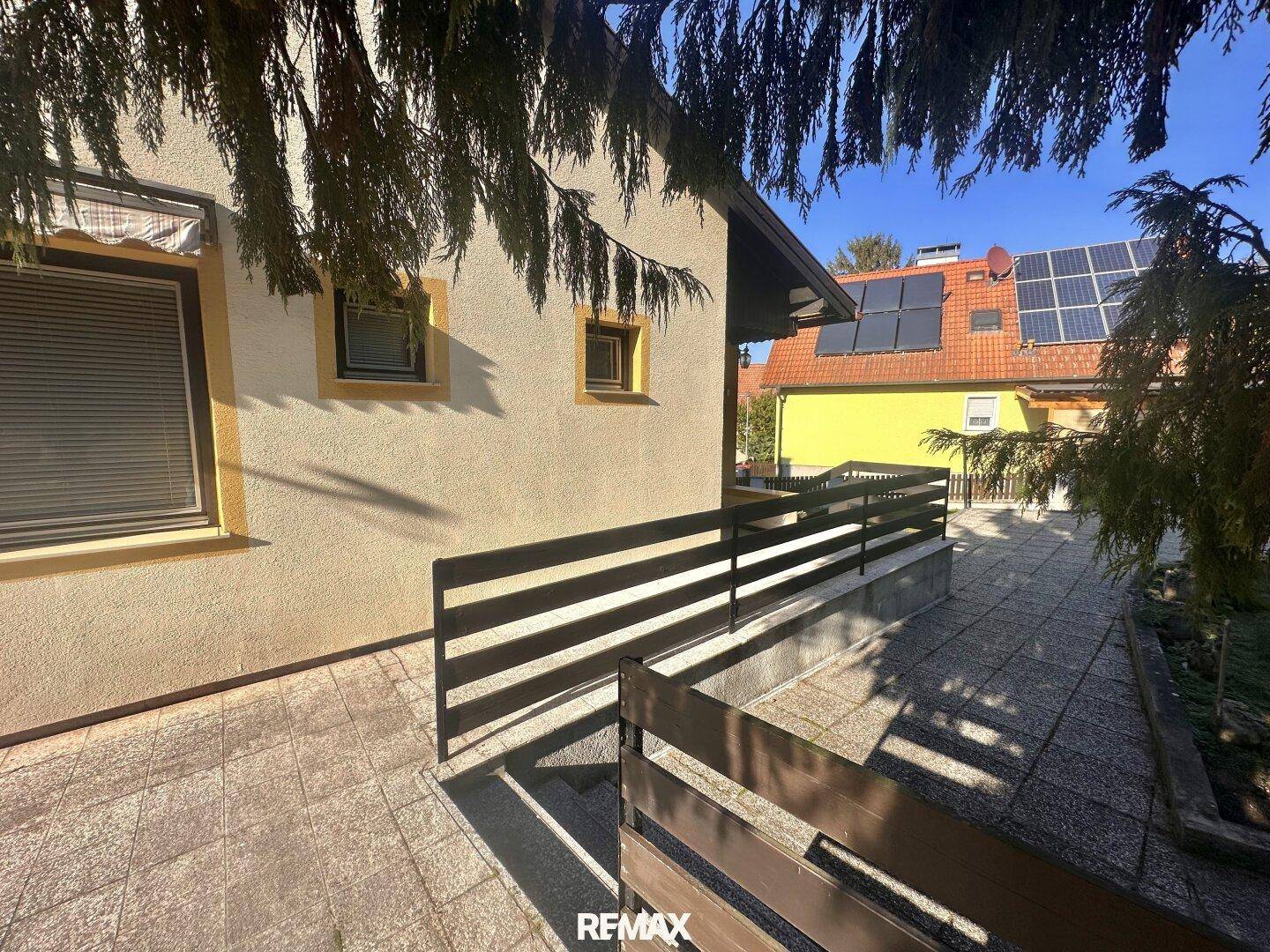 Gedeckter Außenbereich mit Treppe und Geländer, angrenzend an das Haus mit Solaranlage.
