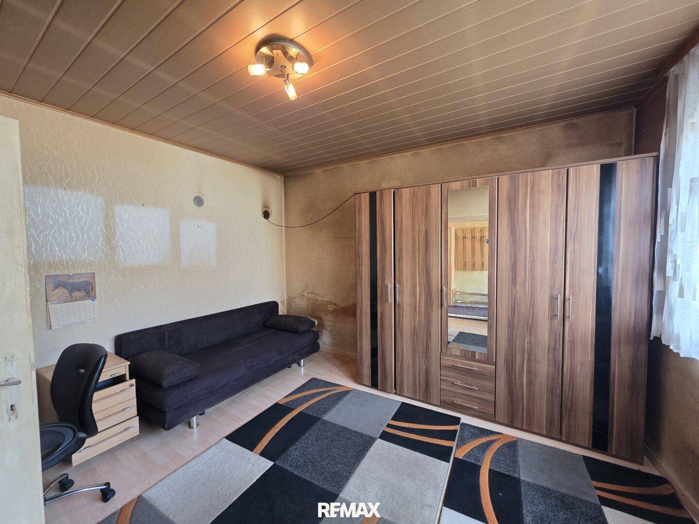 Schlafzimmer mit Holzdecke, Kleiderschrank mit Spiegeln und einem Schlafsofa.