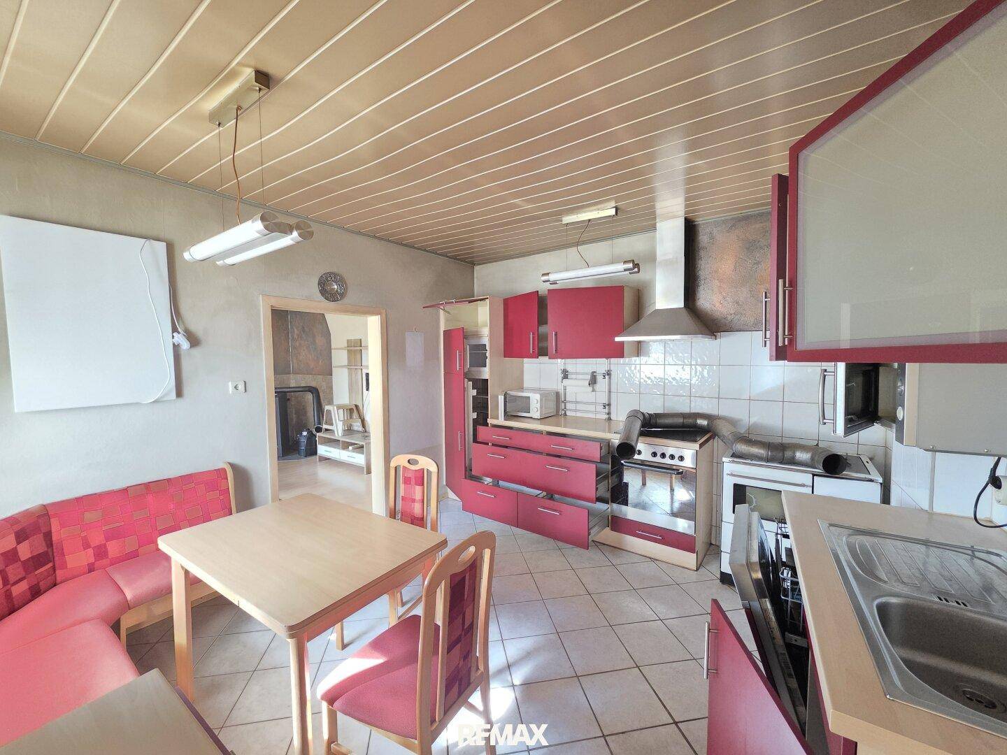 Küche mit roten Schränken, Fliesenboden und Essbereich, bereit zur Modernisierung.
