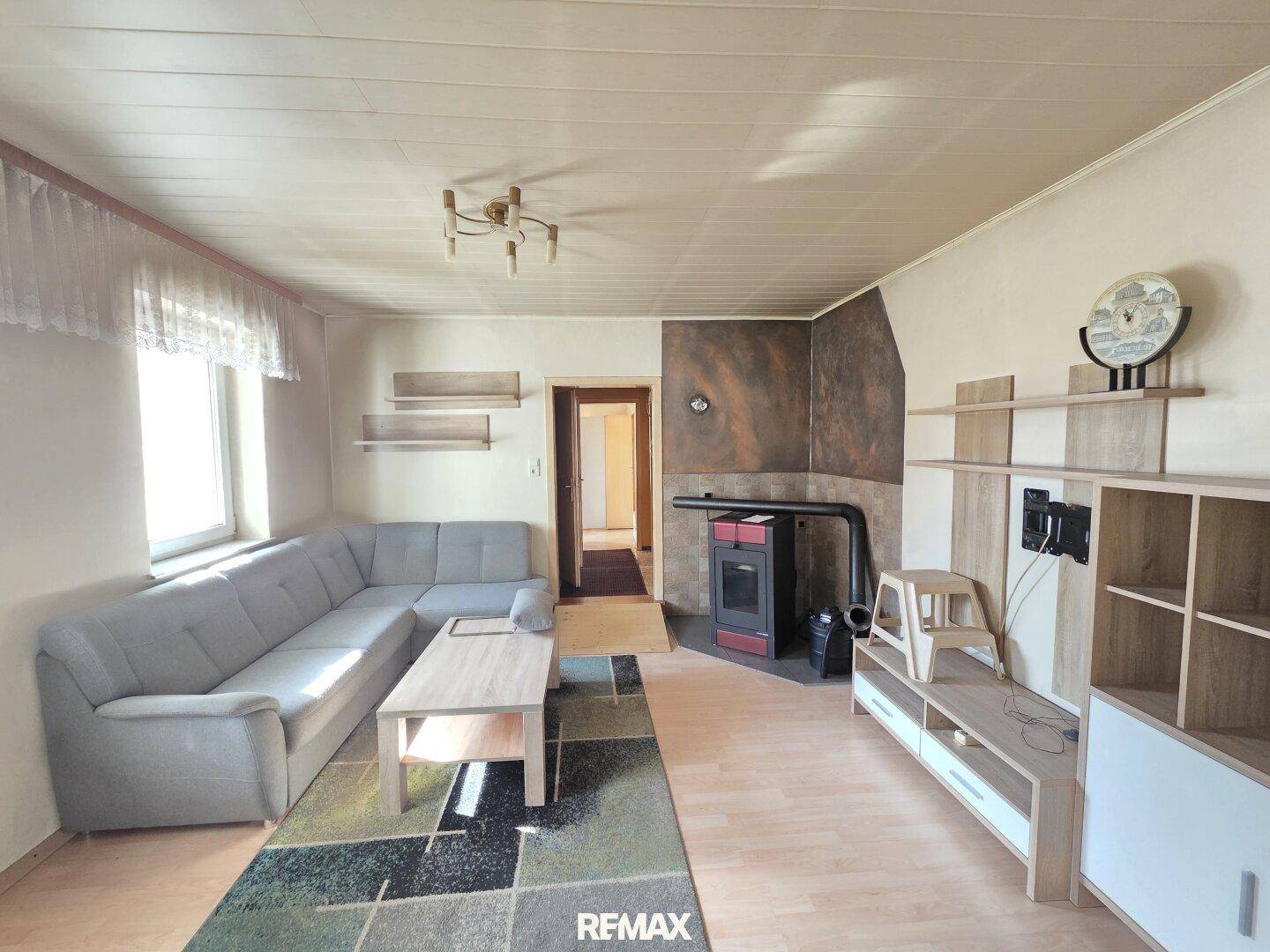 Gemütliches Wohnzimmer mit Ecksofa, Holzofen und Laminatboden, ideal zum Entspannen.