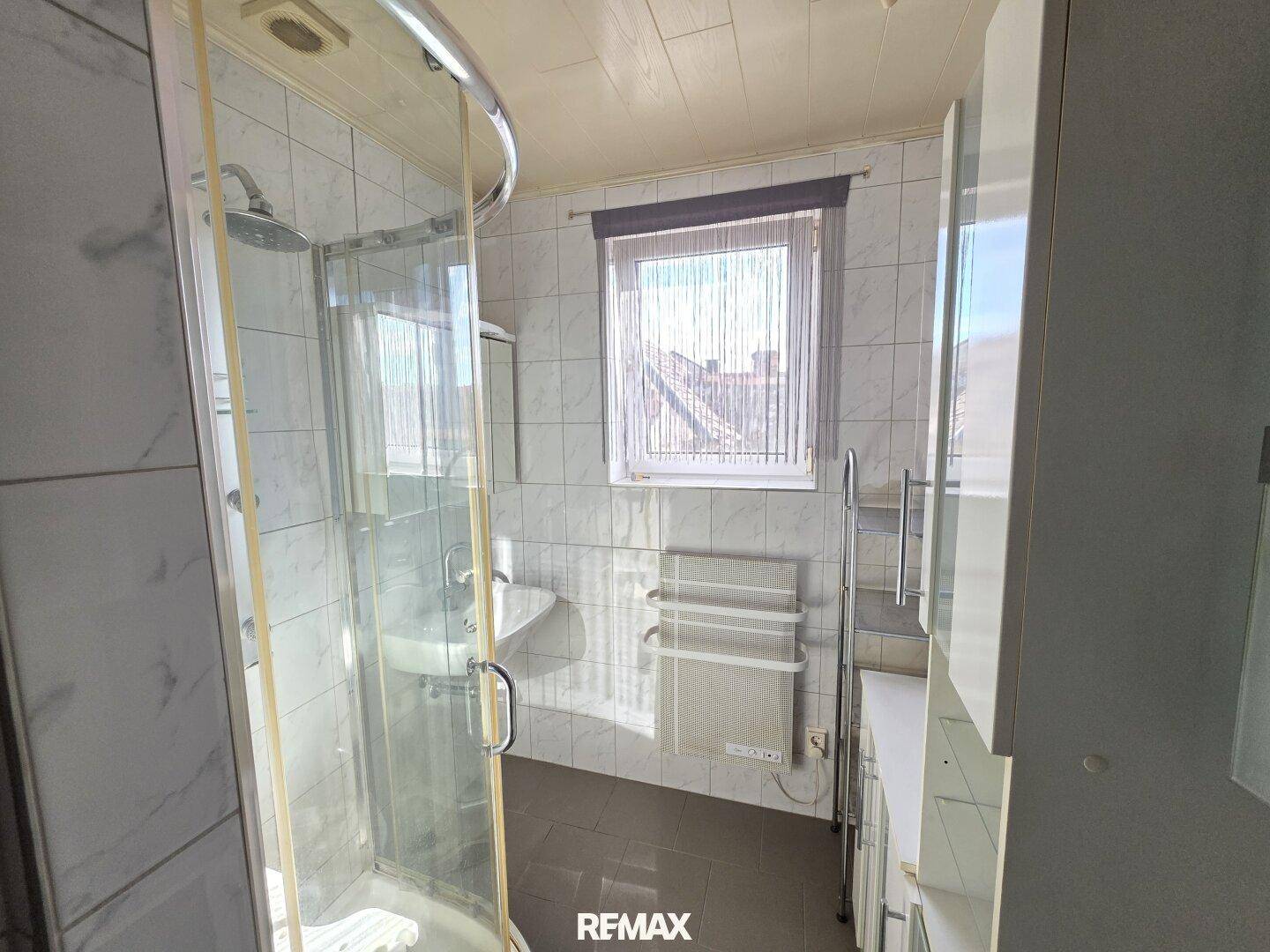 Helles Badezimmer mit Duschkabine, Waschbecken und Fenster, funktional eingerichtet.