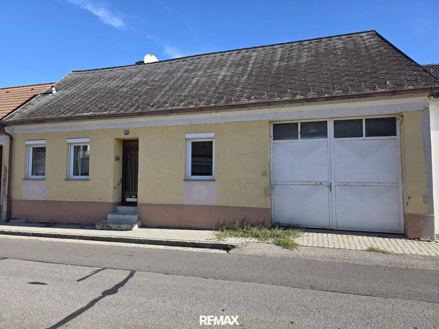 Fassade eines älteren Hauses mit Garage und einfacher Gestaltung an einer ruhigen Straße.