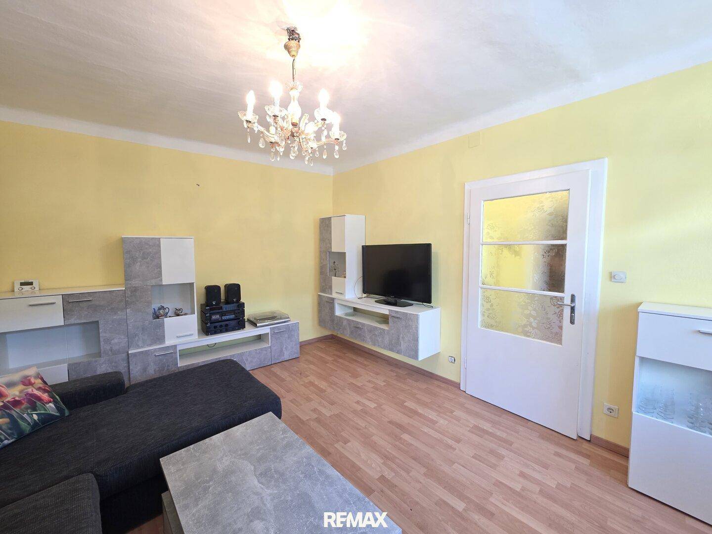 Wohnzimmer mit modernem Sofa, TV-Möbeln und einem Kronleuchter an der Decke.