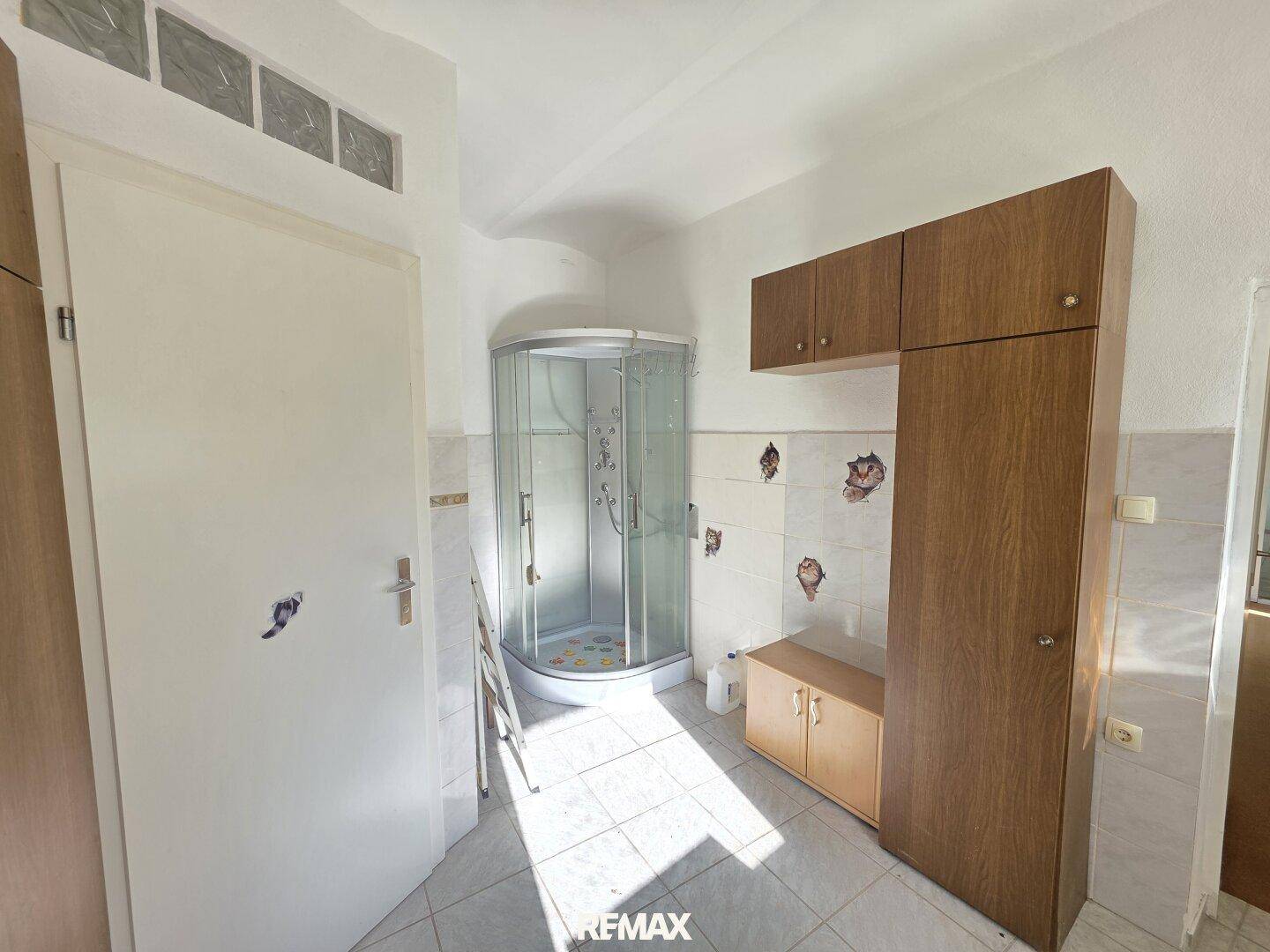 Badezimmer mit Duschkabine und Holzschränken, die viel Stauraum bieten.