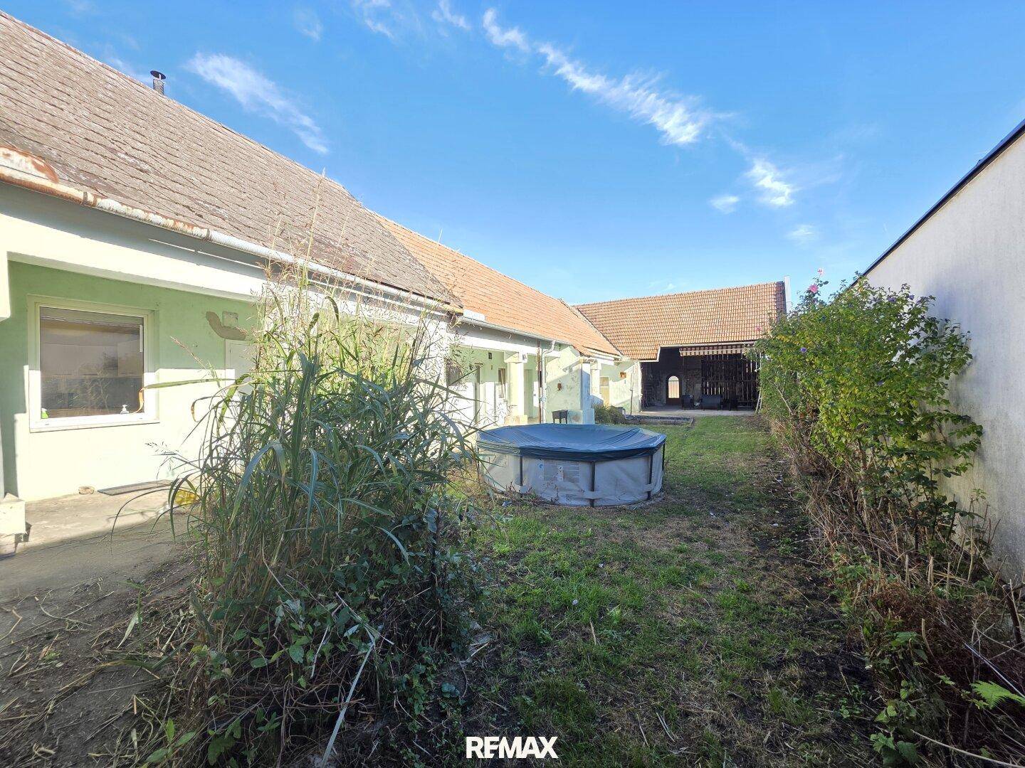 Hinterhof mit einem aufgestellten Pool und üppiger Vegetation unter blauem Himmel.