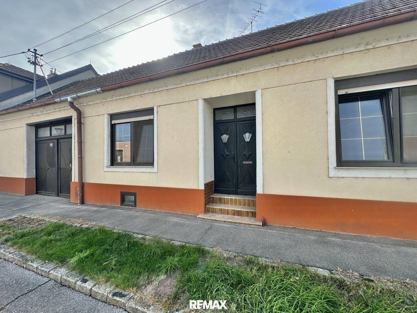 Fassade eines Hauses von der Straße aus gesehen, mit Fenstern und einer Eingangstür.