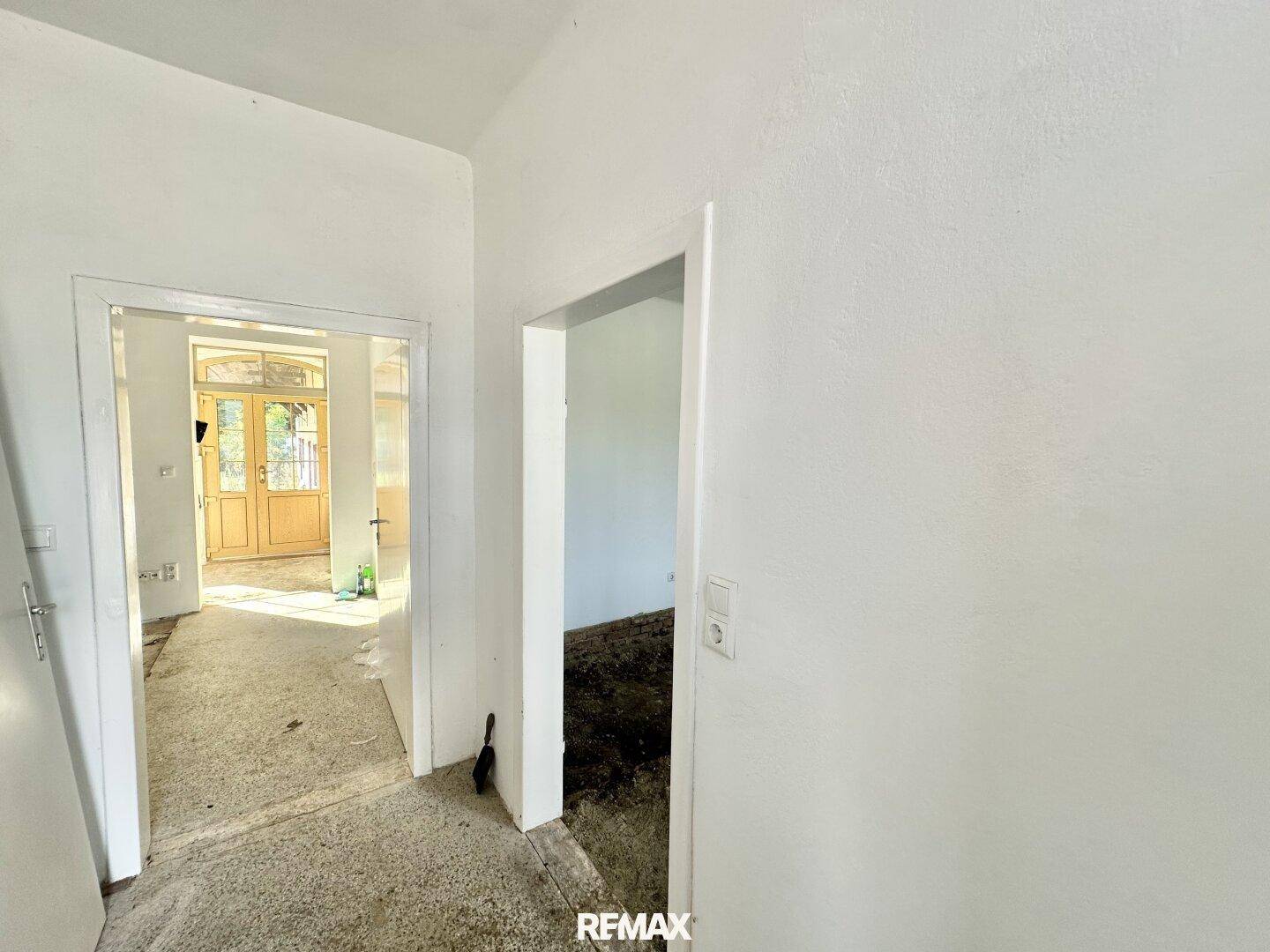 Flur mit weißen Wänden und unfertigem Boden, der zu weiteren Räumen im Haus führt.