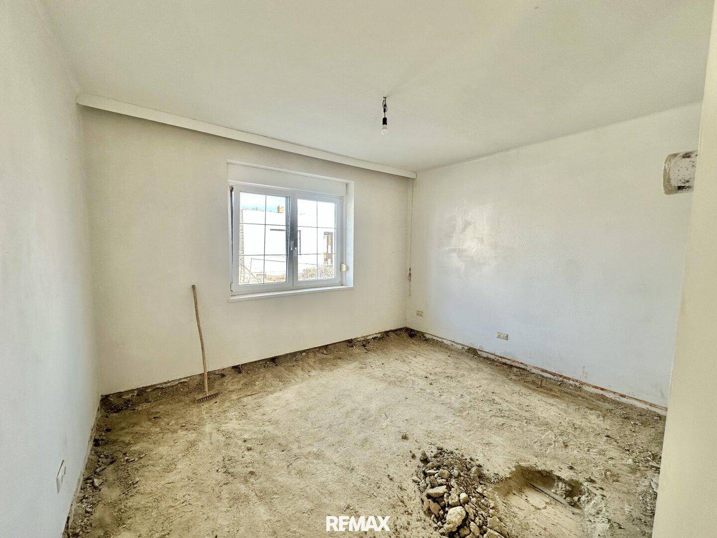 Weiterer Innenraum mit weißen Wänden und Fenster, dessen Boden entfernt wurde und eine Renovierung benötigt.