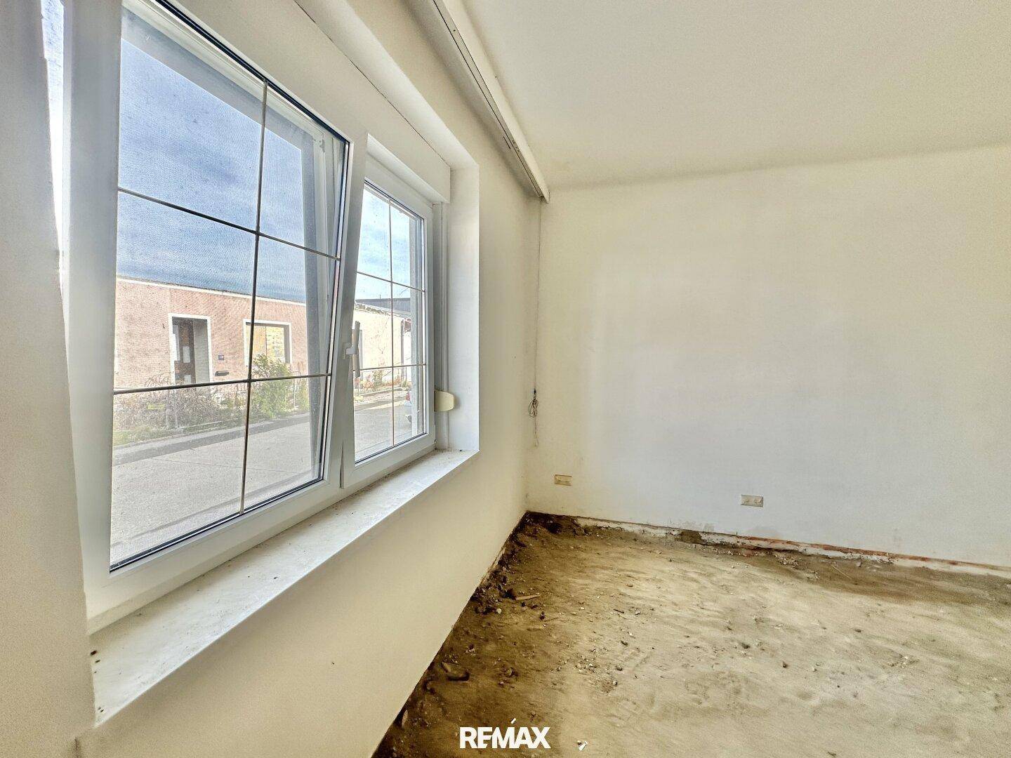 Innenraum mit großem Fenster und weißen Wänden, der sich in einem unfertigen Zustand befindet und renovierungsbedürftig ist.