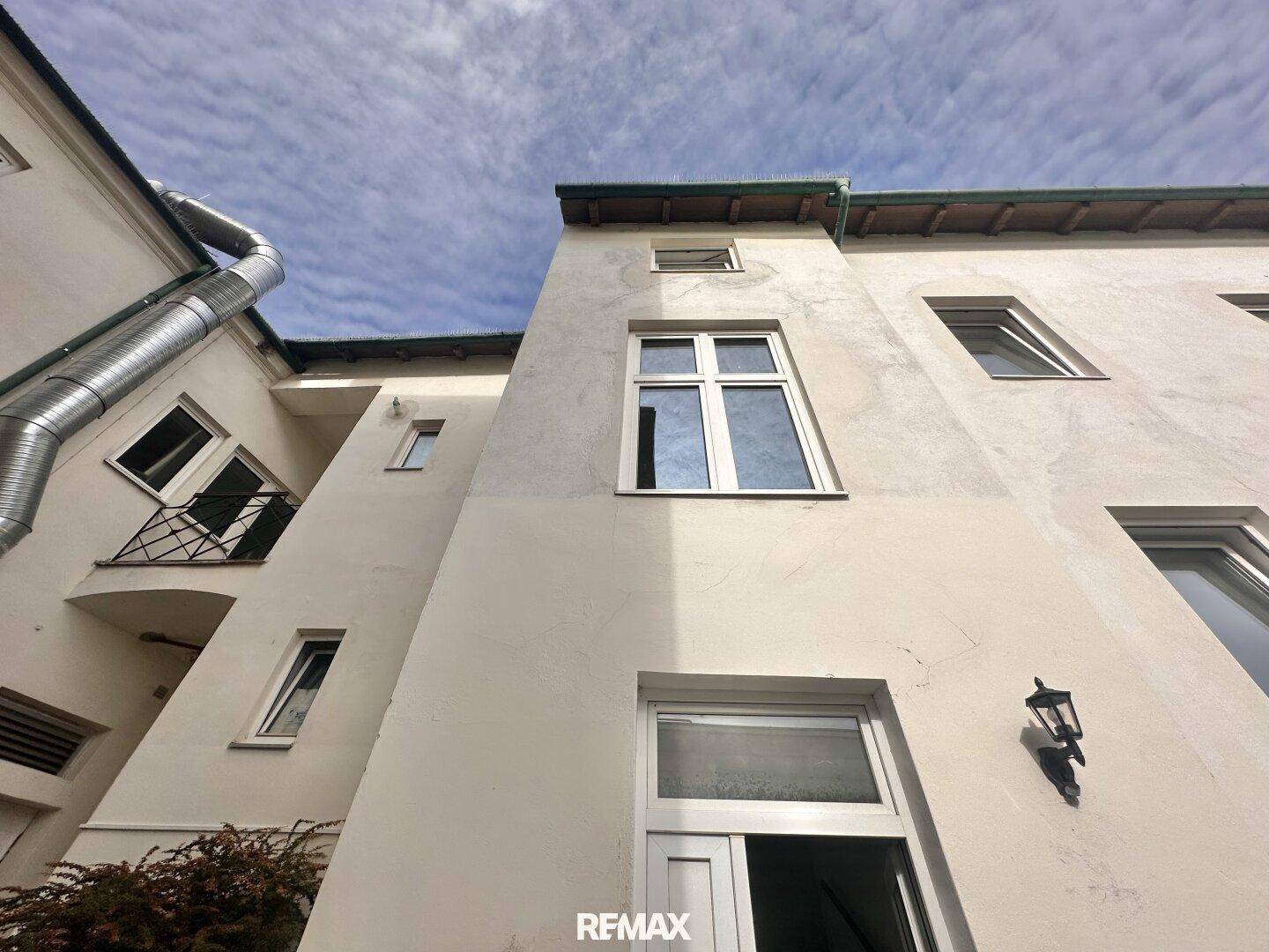 Rückansicht eines Gebäudes mit mehreren Fenstern und einem Balkon unter blauem Himmel.