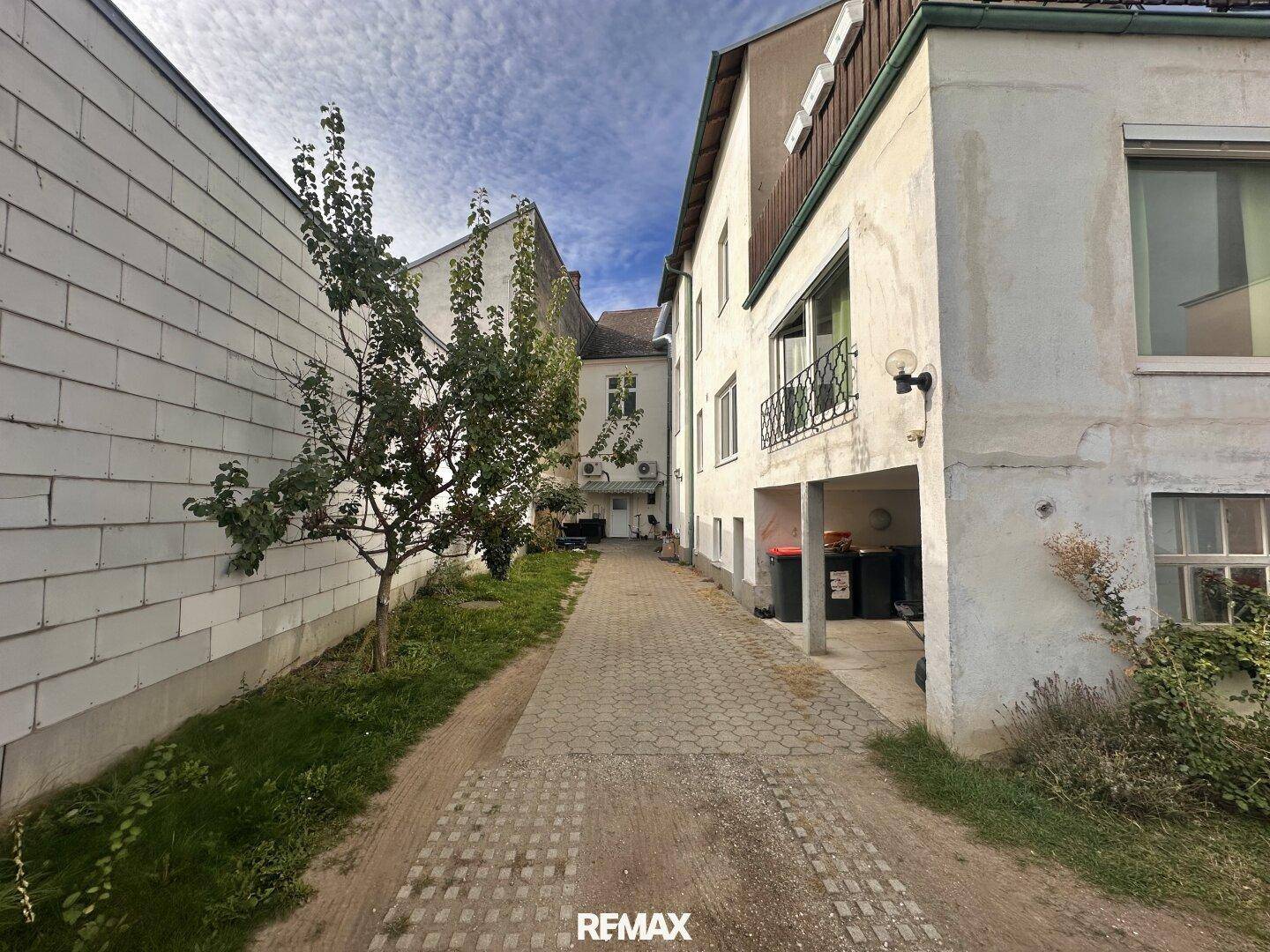 Gepflasterter Hinterhofweg mit Gebäuden und einem überdachten Bereich für Mülltonnen.