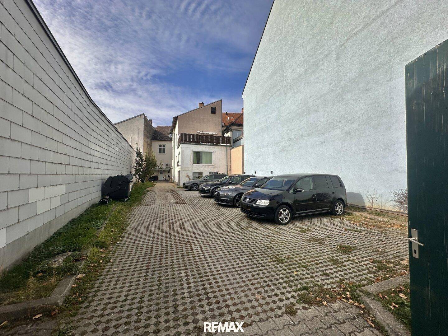 Parkplatz mit gepflasterter Fläche und mehreren Autos zwischen Gebäuden.