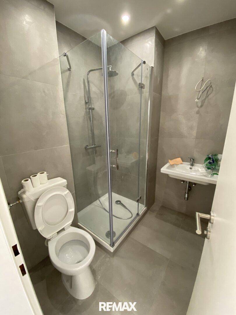 Modernes Badezimmer mit grauen Fliesen, Duschkabine und Toilette.