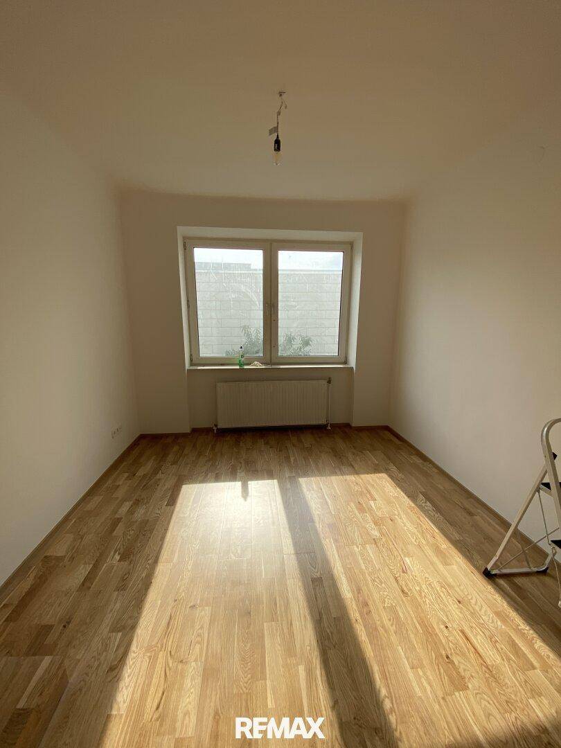 Heller Raum mit neuem Parkettboden und einem Fenster, das viel Tageslicht hereinlässt.