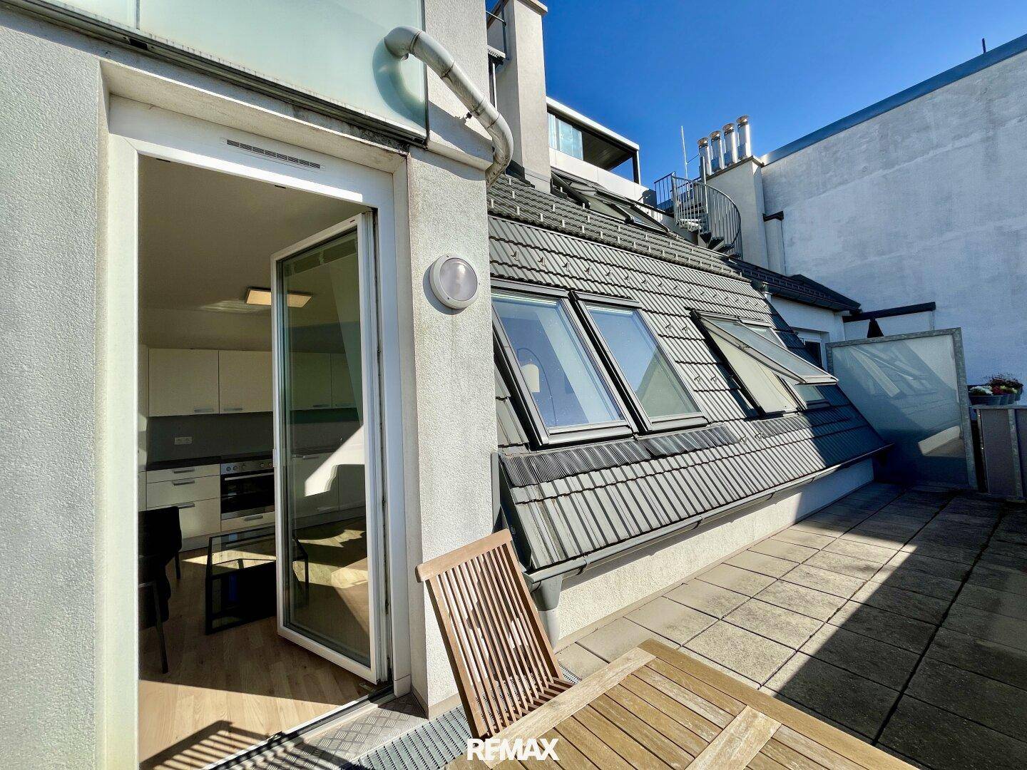 Geräumige Dachterrasse mit Fliesen- und Holzbelag, direktem Zugang zum Innenbereich und Dachfenstern.