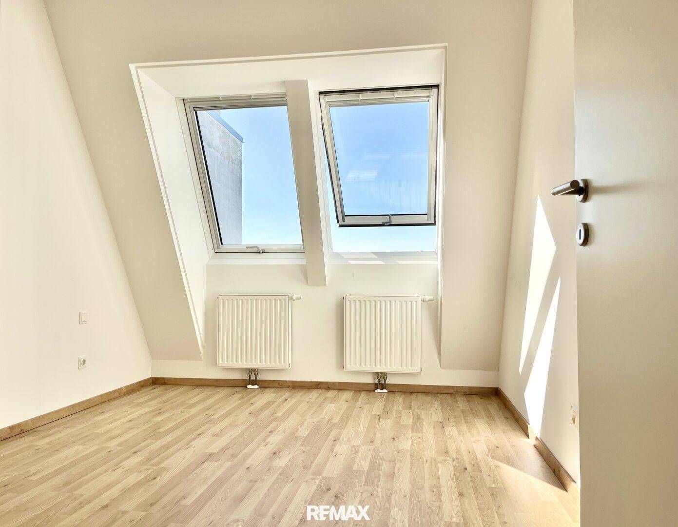 Helles Zimmer mit Dachschrägen, zwei großen Dachfenstern und Holzboden.