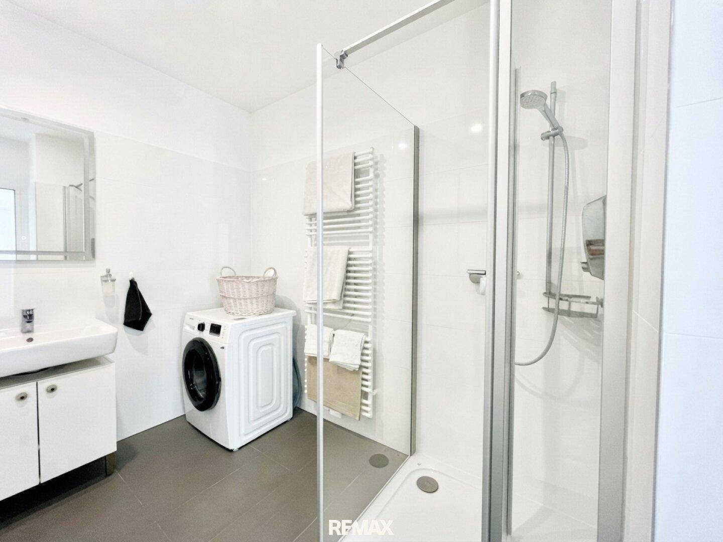 Modernes Badezimmer mit Dusche, Waschbecken, beheiztem Handtuchhalter und Waschmaschine.
