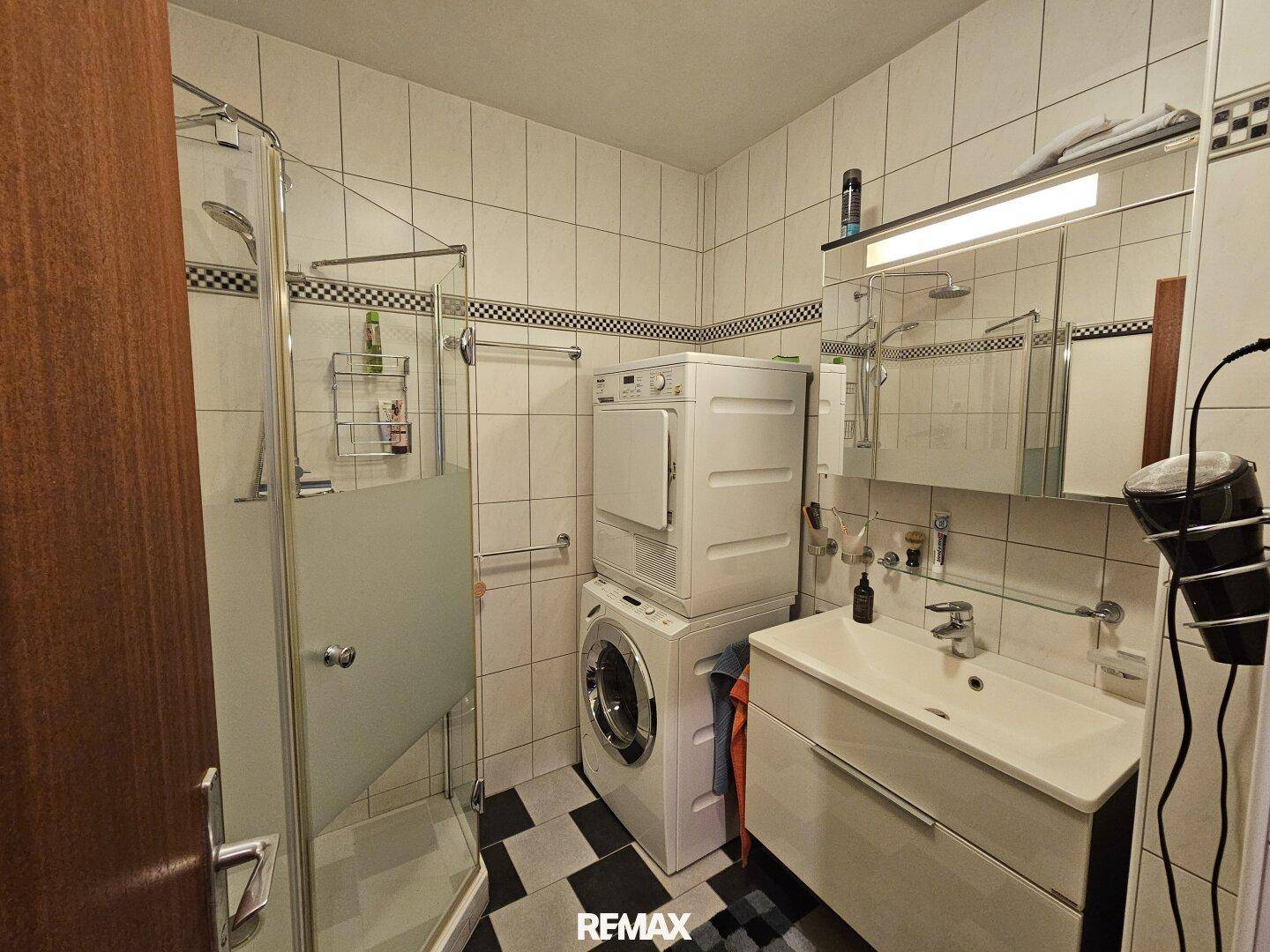 Modernisiertes Badezimmer mit Dusche, Waschmaschine und Trockner, sowie einem Einzelwaschbecken.