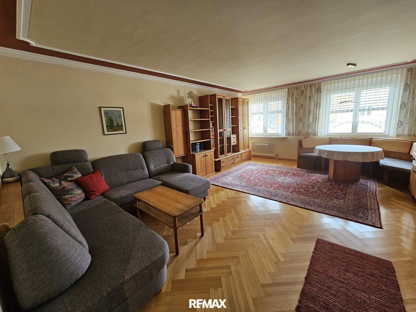 Geräumiges Wohnzimmer mit Fischgrätparkett, großer Couch und traditionellen Holzmöbeln.