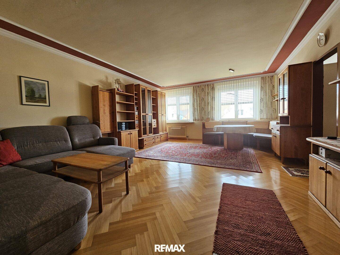 Klassisches Wohnzimmer mit beigem Sofa, Holzmöbeln und einem großen Teppich.