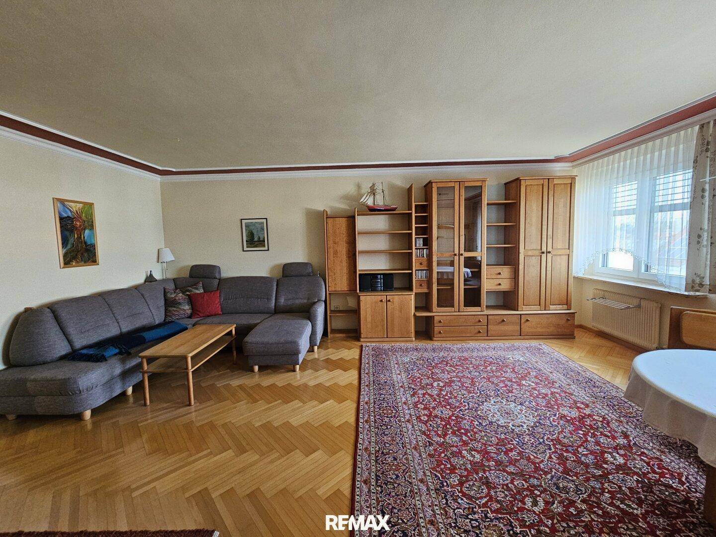 Helles Wohnzimmer mit Parkettboden, bequemer Couch und Blick auf die Fenster.