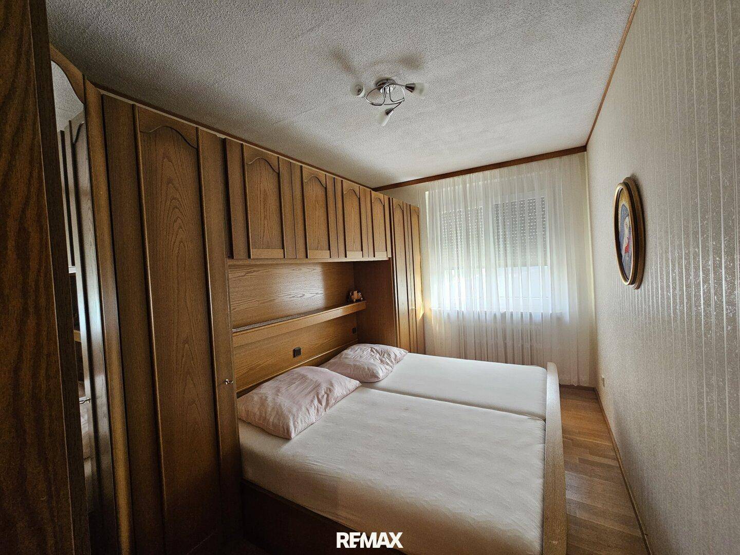 Schlafzimmer mit zwei Einzelbetten, Holzschränken und einem Fenster mit Vorhängen.
