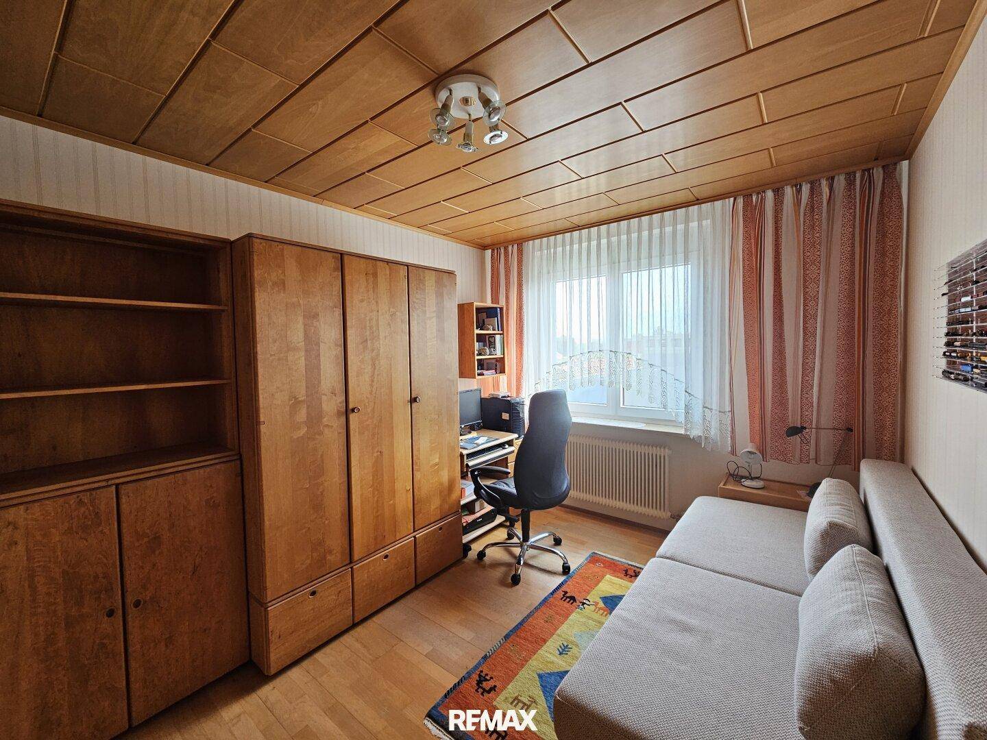 Helles Arbeitszimmer mit Holzdecke, Schreibtisch und großem Kleiderschrank.