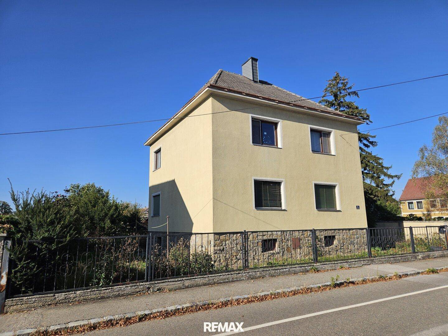Seitenansicht des gelben Hauses mit gepflegtem Vorgarten und klarem Himmel.