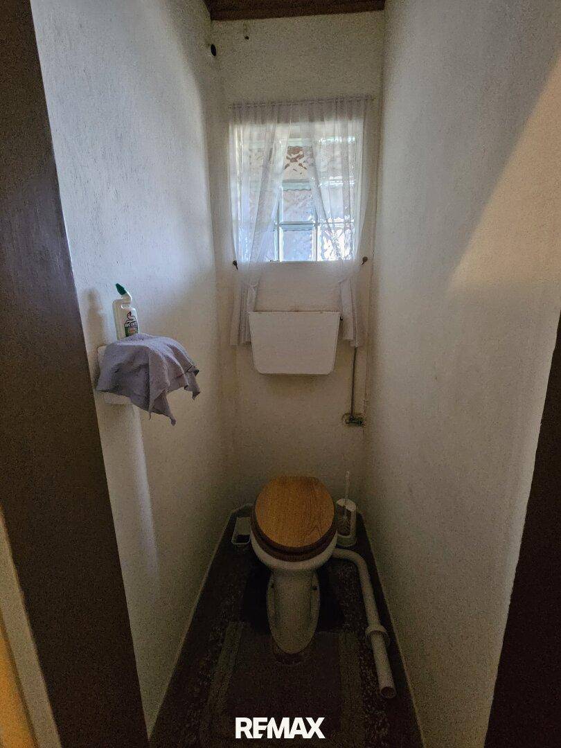 Kleines Gäste-WC mit Toilette, Fenster und gemusterten Tapeten im Originalzustand.