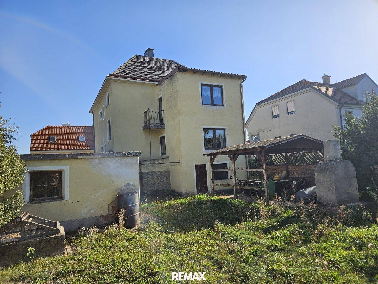 Rückseite des Hauses mit überdachtem Sitzbereich und großem Garten.