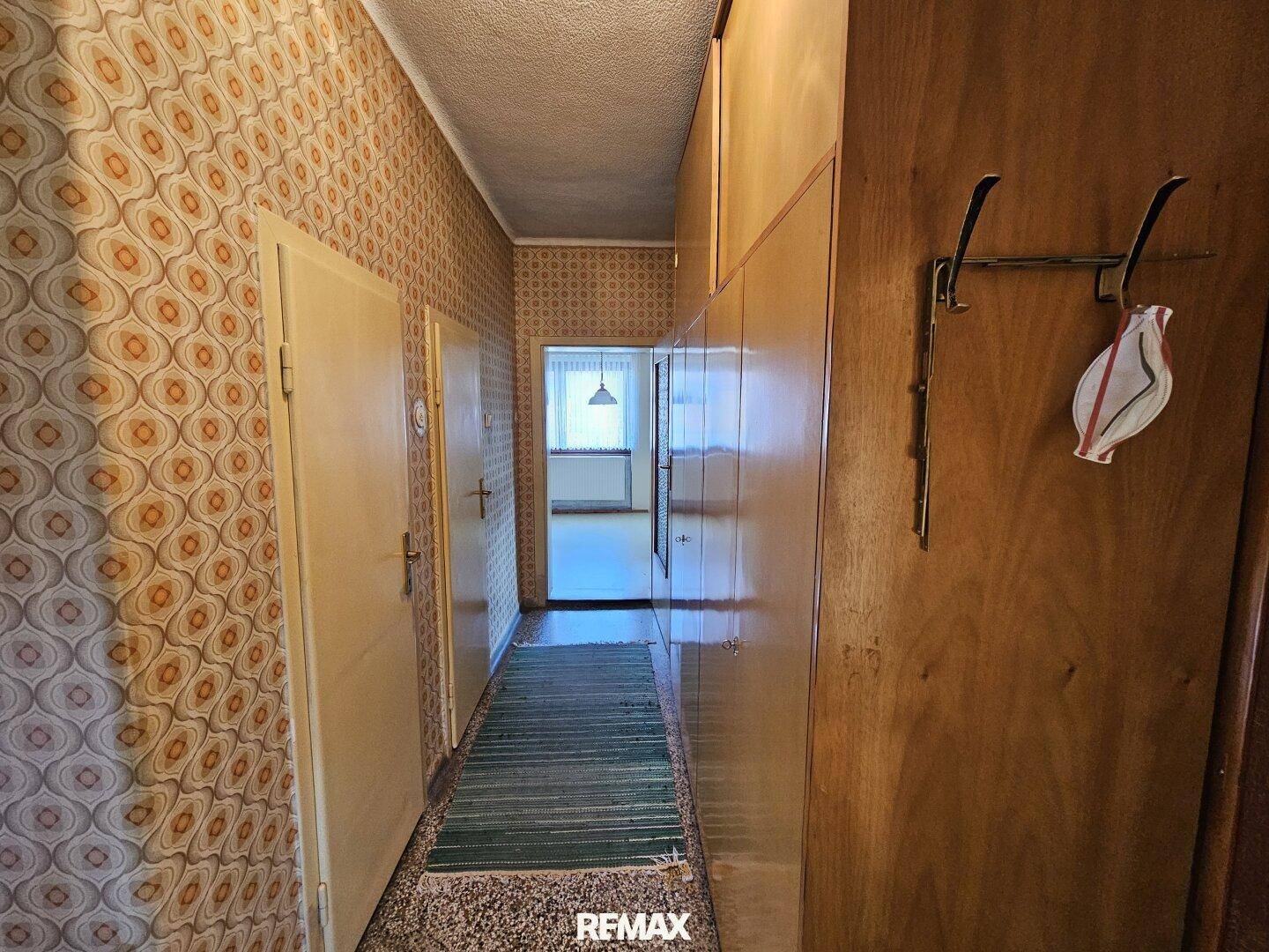 Langer Flur mit Garderobe, Holzschränken und gemusterten Tapeten.