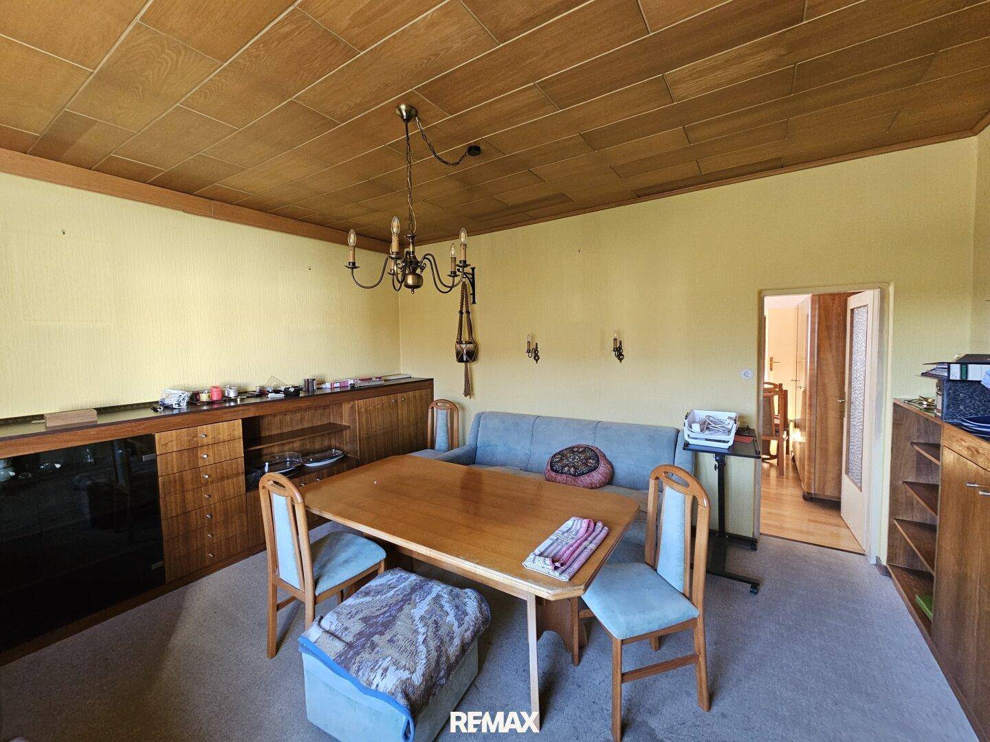 Offener Wohn-Essbereich mit Holztisch, Sofa und Holzdeckenverkleidung.