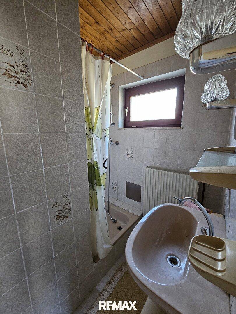Badezimmer mit Dusche, Waschbecken, Holzdecke und Fliesen an den Wänden.