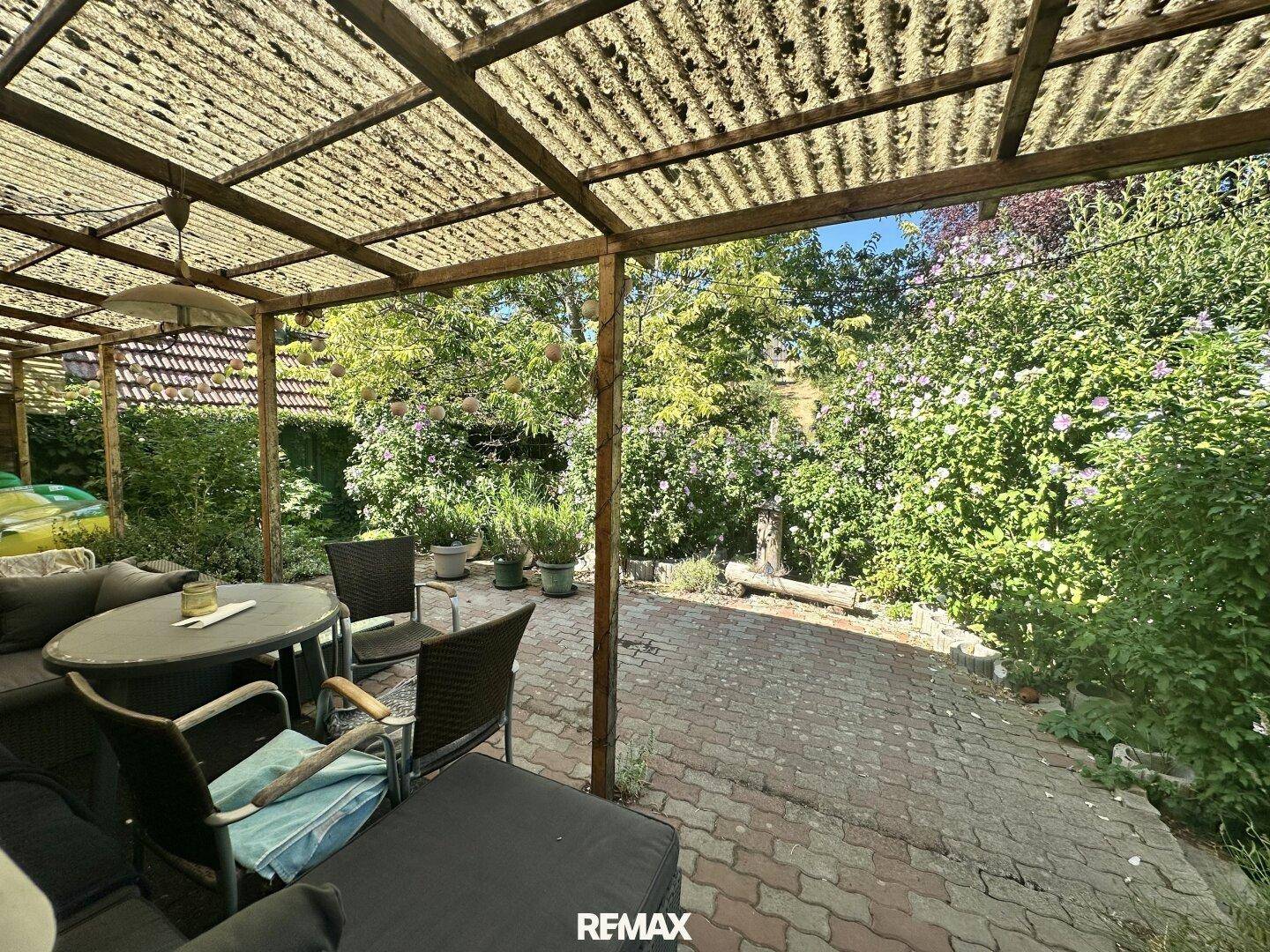 Überdachte Terrasse mit Sitzgelegenheiten und Blick auf den grünen Gartenbereich.