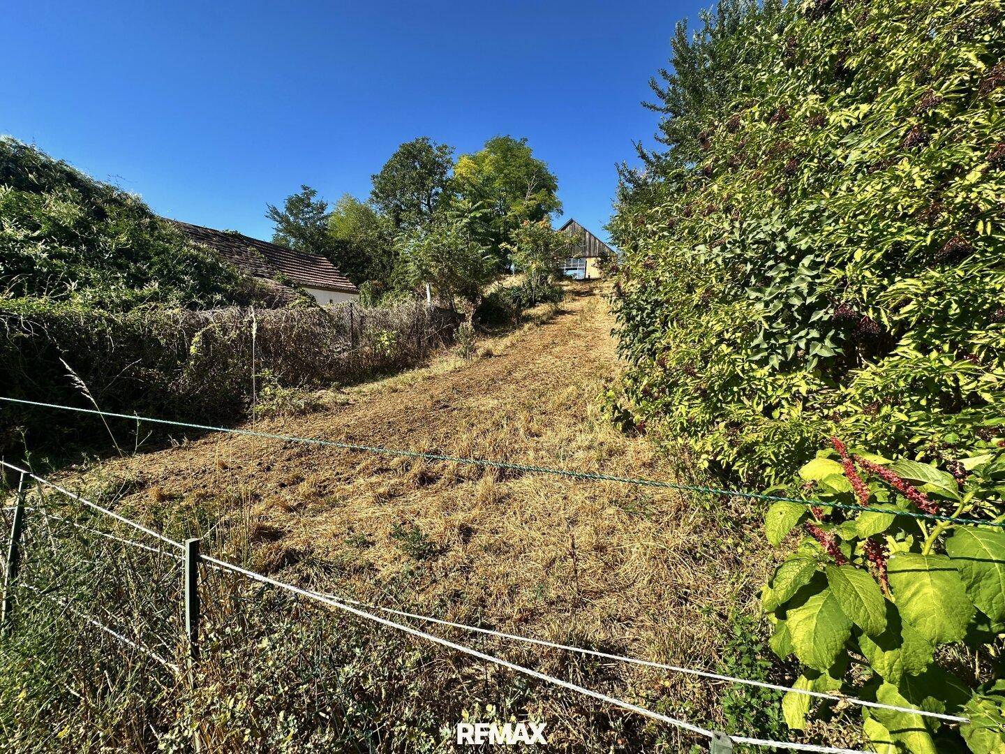 Weitläufiges Grundstück mit trockenem Gras und umzäuntem Bereich unter blauem Himmel.