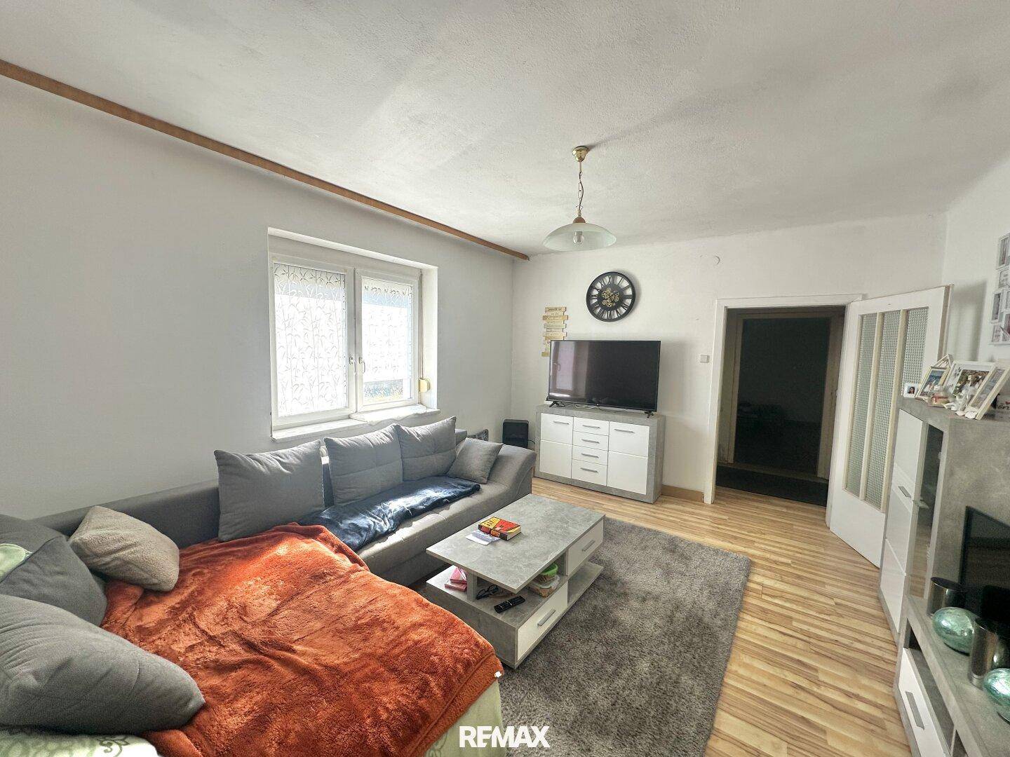 Helles Wohnzimmer mit beigem Laminatboden, grauem Sofa und modernem TV-Möbel.