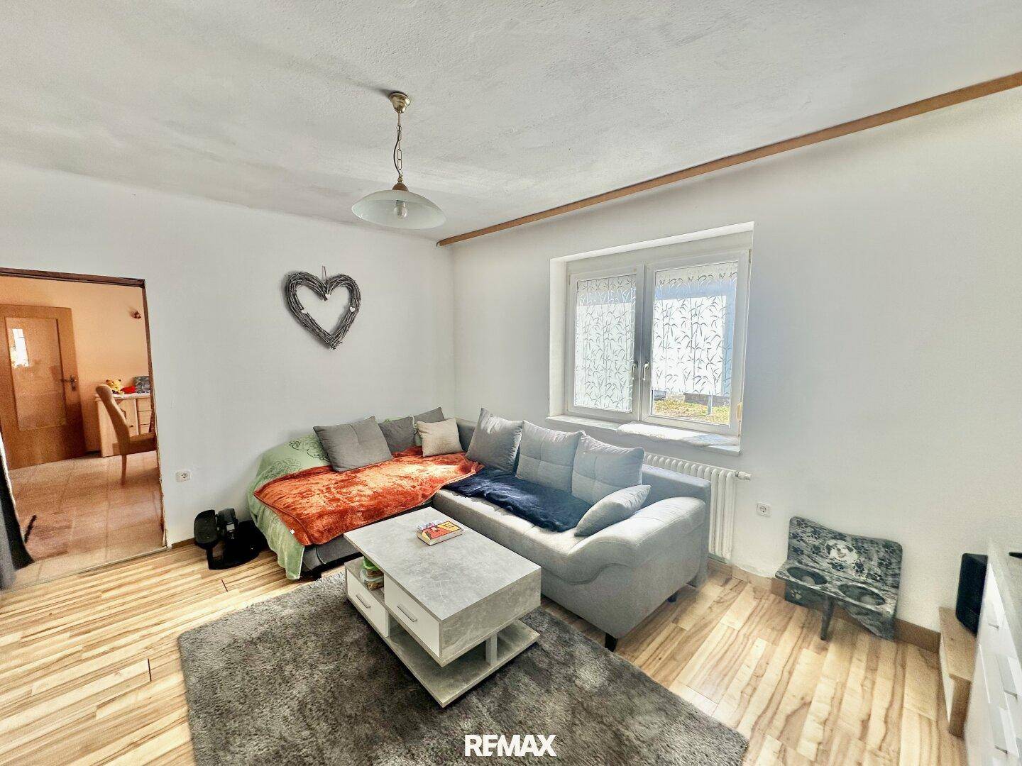 Gemütliches Wohnzimmer mit L-förmigem Sofa, Teppich und Blick nach draußen.
