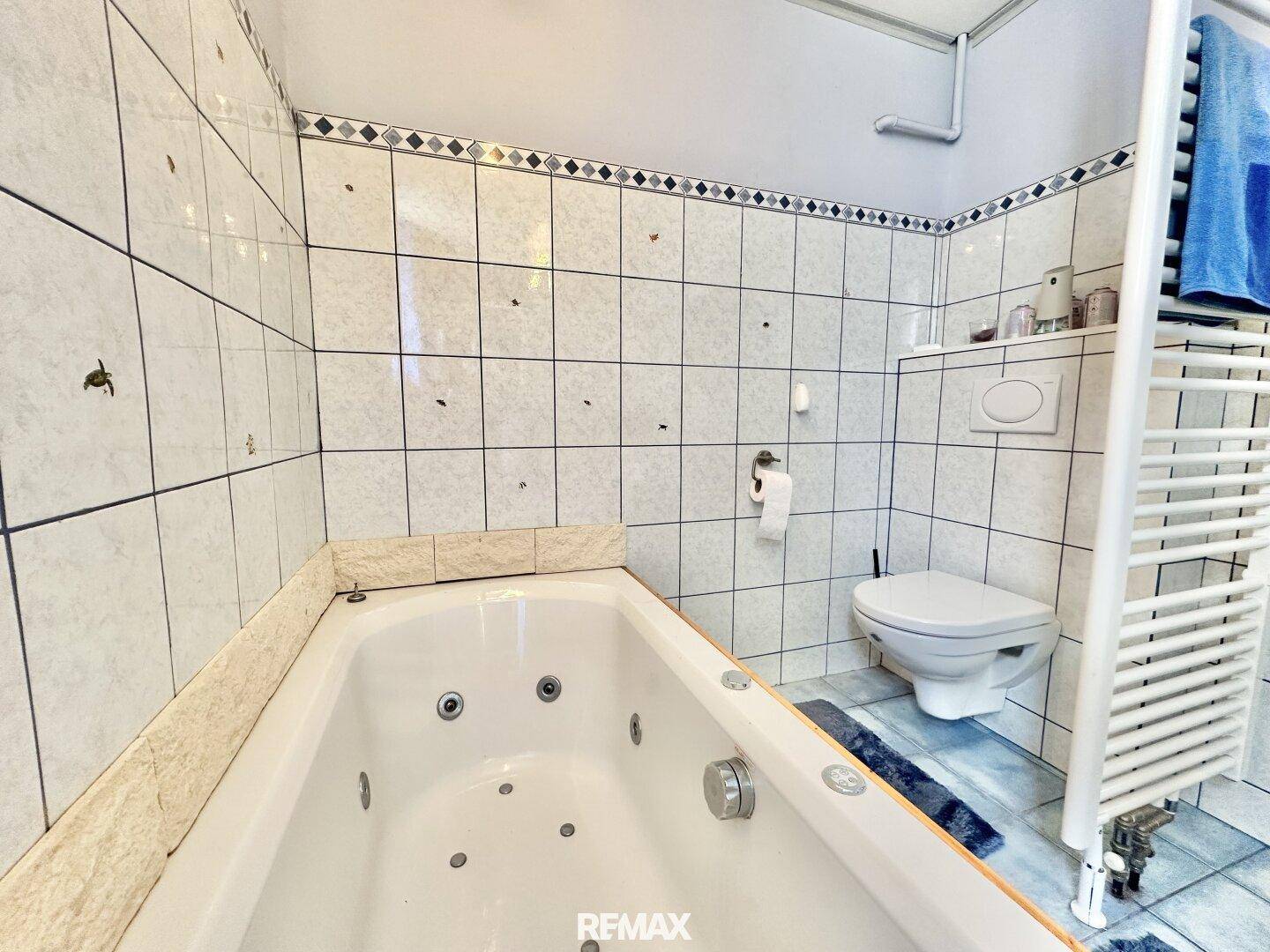 Badezimmer mit Whirlpool-Badewanne, Toilette und Fliesen in Hellblau und Weiß.