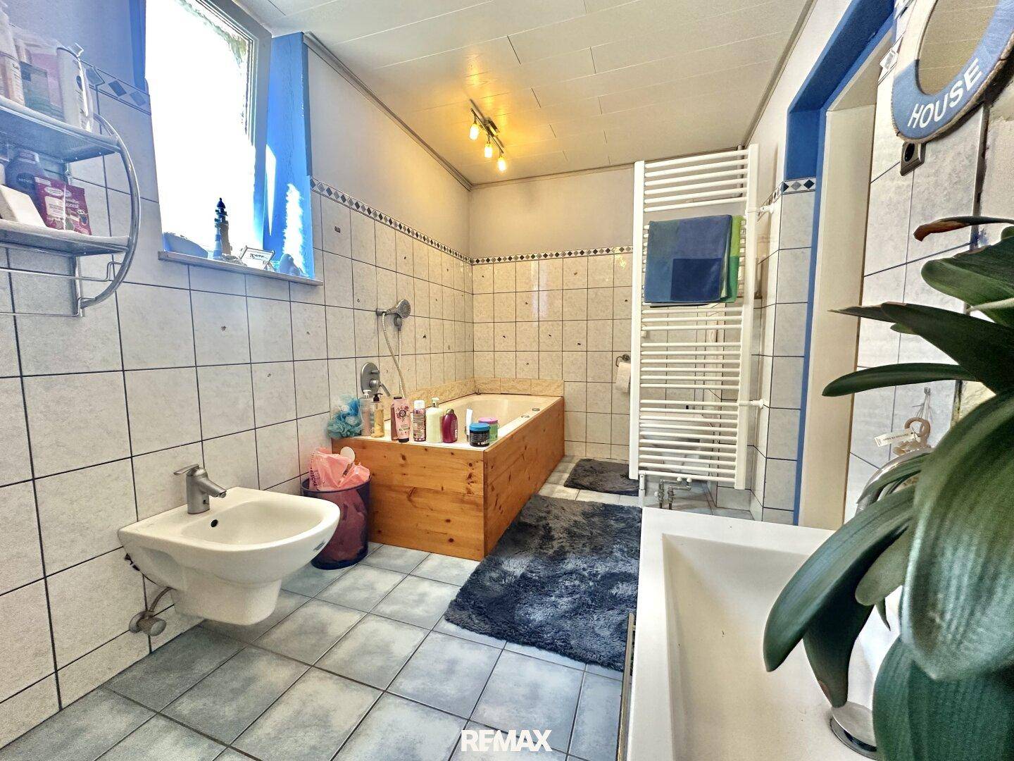 Gefliestes Badezimmer mit Badewanne, Bidet und großem Fenster für Tageslicht.