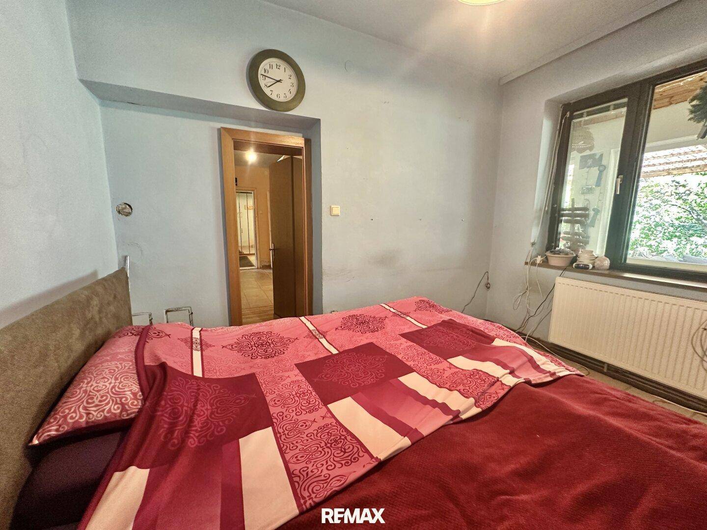 Schlafzimmer mit Doppelbett, roter Bettwäsche und Fenster mit Blick nach draußen.