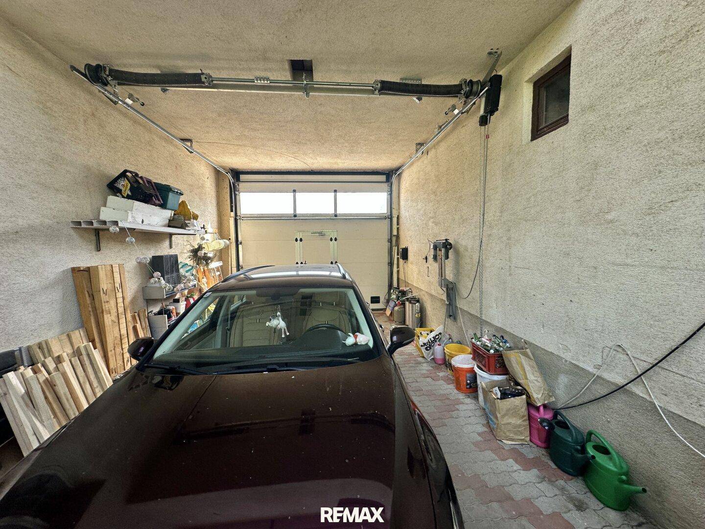 Geräumige Garage mit einem geparkten Auto und Stauraum an den Wänden und Deckenkonstruktion.