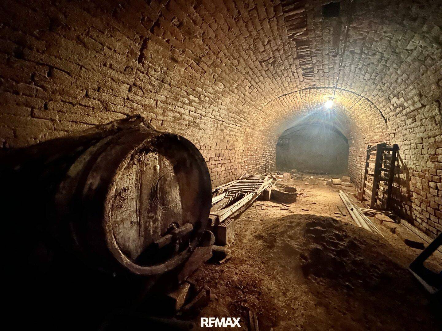 Historischer Weinkeller mit Ziegelgewölbe, großem Holzfass und gedämpfter Beleuchtung.