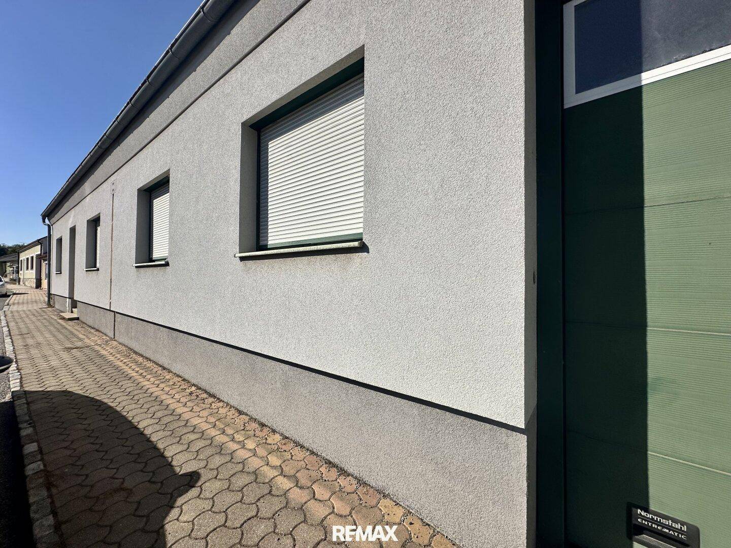 Moderne Gebäudefassade mit grauer Putzfassade, Fenstern und Rollläden unter blauem Himmel.