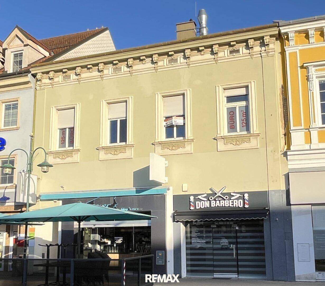 Fassade eines historischen Gebäudes mit Geschäften und Büros, beleuchtet von der Morgensonne.