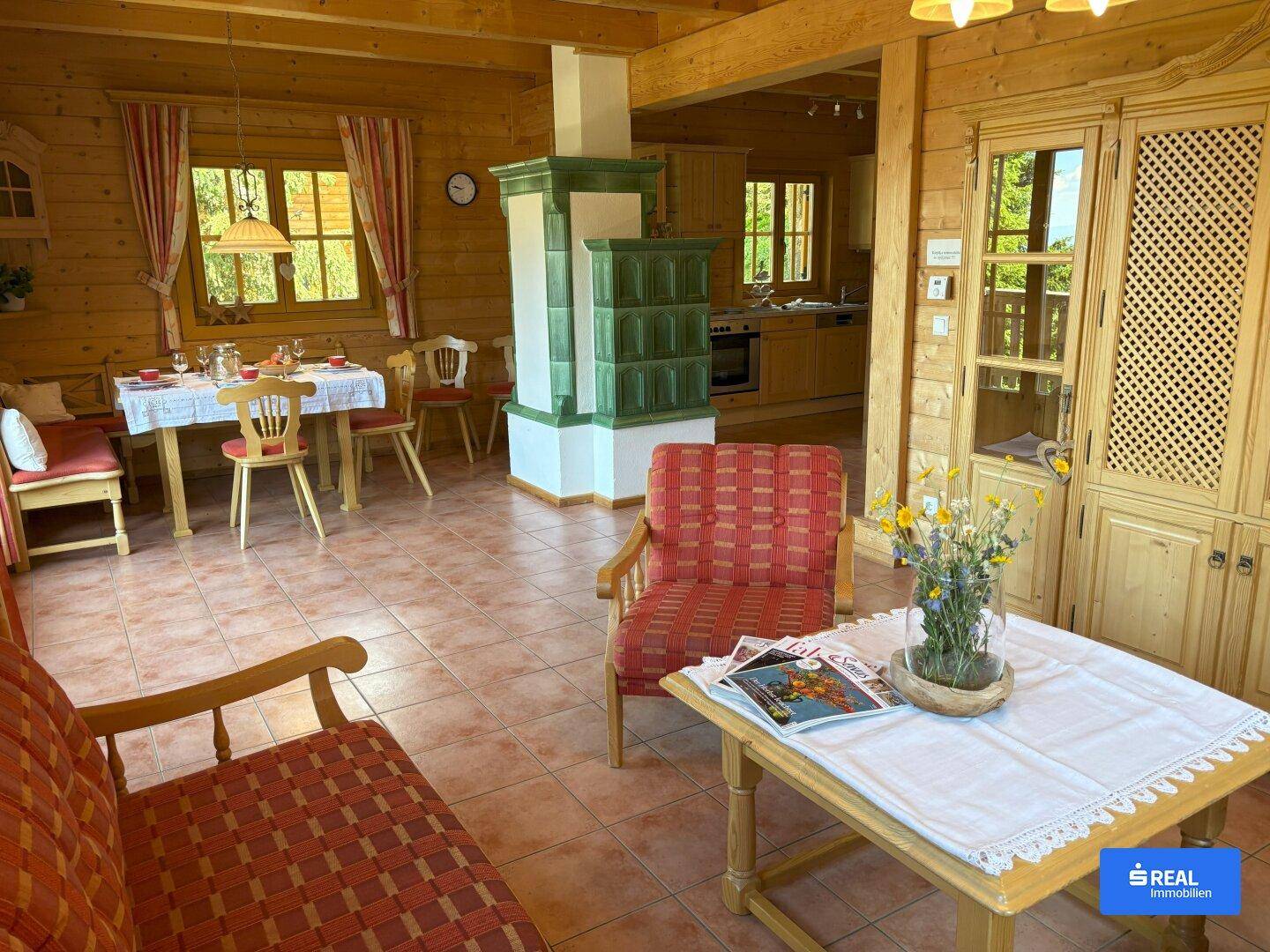 Offener Wohn- und Essbereich mit traditionellem Kachelofen, Holzelementen und Blick zur Küche.
