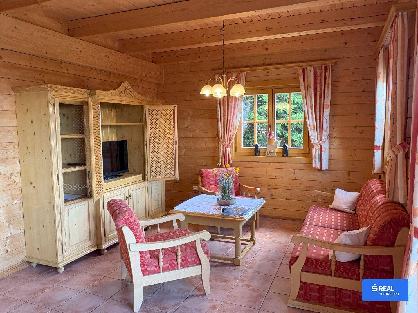 Gemütliches Wohnzimmer im Chalet-Stil mit Holzwänden, traditionellen Möbeln und einem Fernseher in einem Holzschrank.