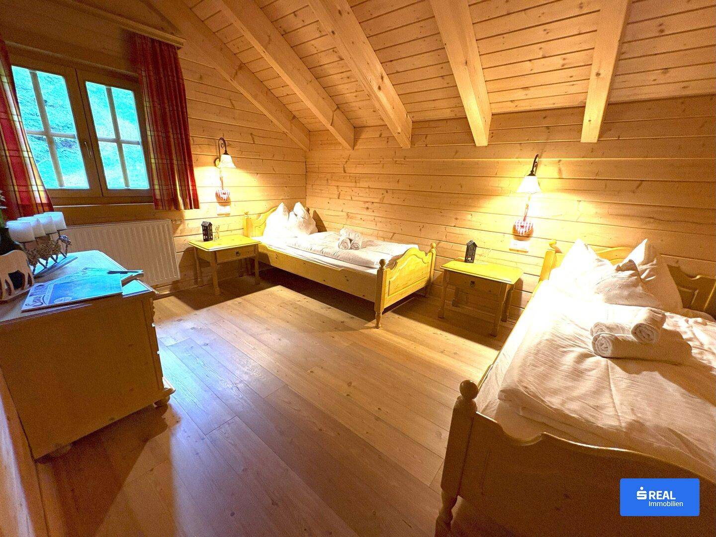 Gemütliches Schlafzimmer mit zwei Einzelbetten, Holzwänden, sichtbaren Deckenbalken und Dachschräge.